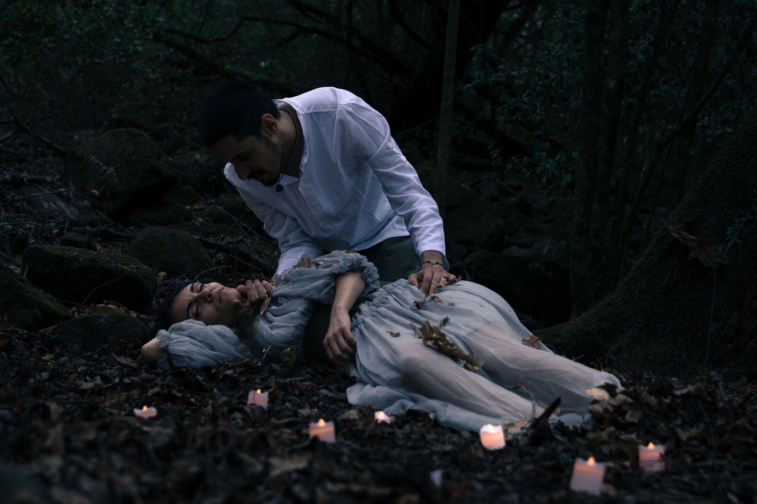 Atmospheric evening photoshoot with candlelight in a dark forest setting.