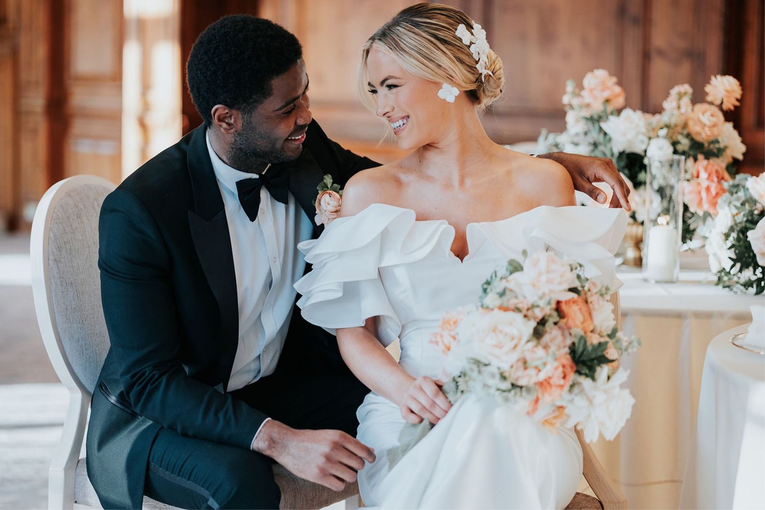 Intimate wedding moment between two people in formal attire with peach florals and decor in an elegant indoor setting.