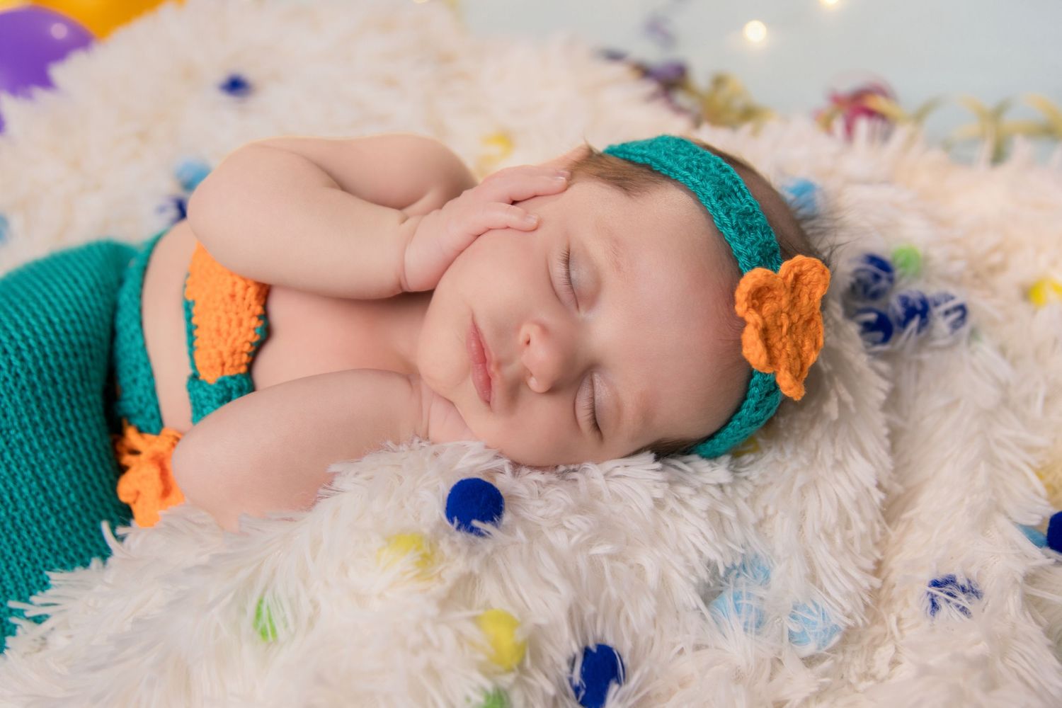 A newborn baby sleeps peacefully on white blankets surrounded by colorful butterflies and floral decorations.