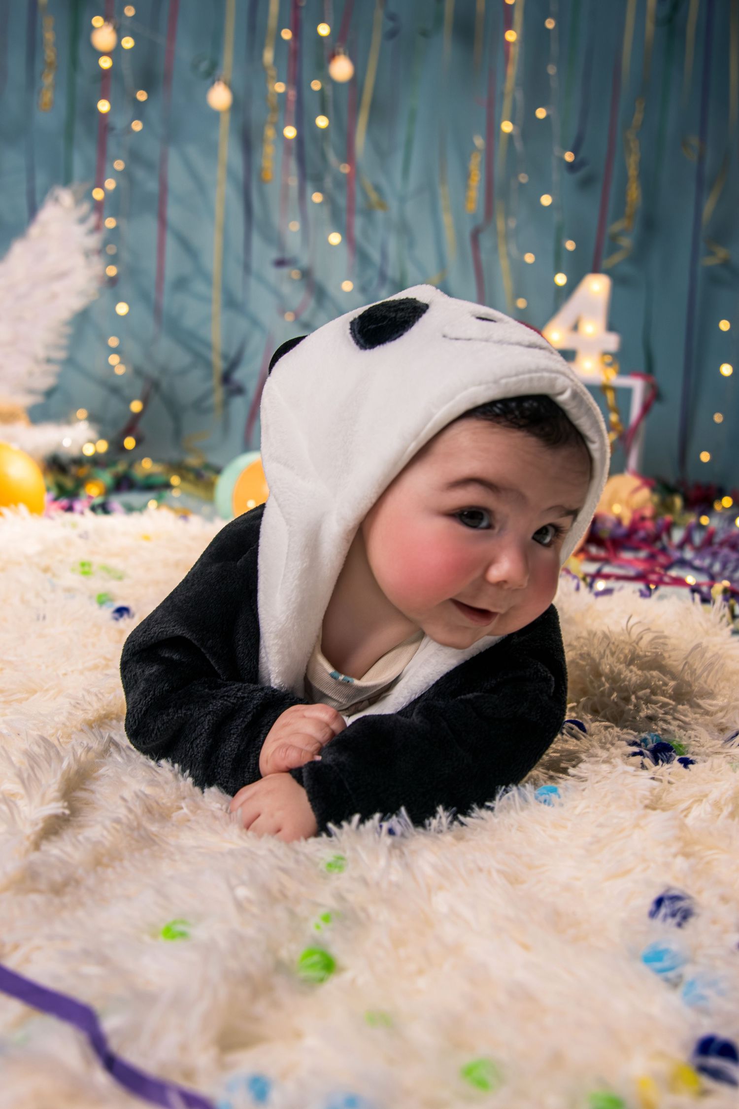 A series of photos showing a baby in a panda costume laying on a soft white blanket with twinkling lights in the background.