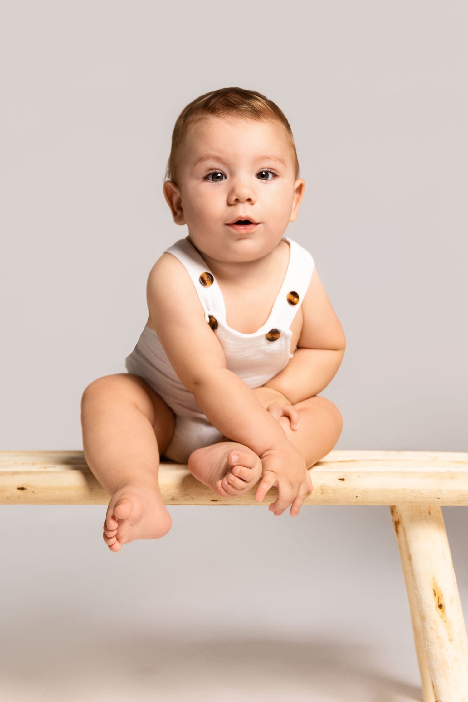 A minimalist studio portrait with a wooden bench against a grey background.