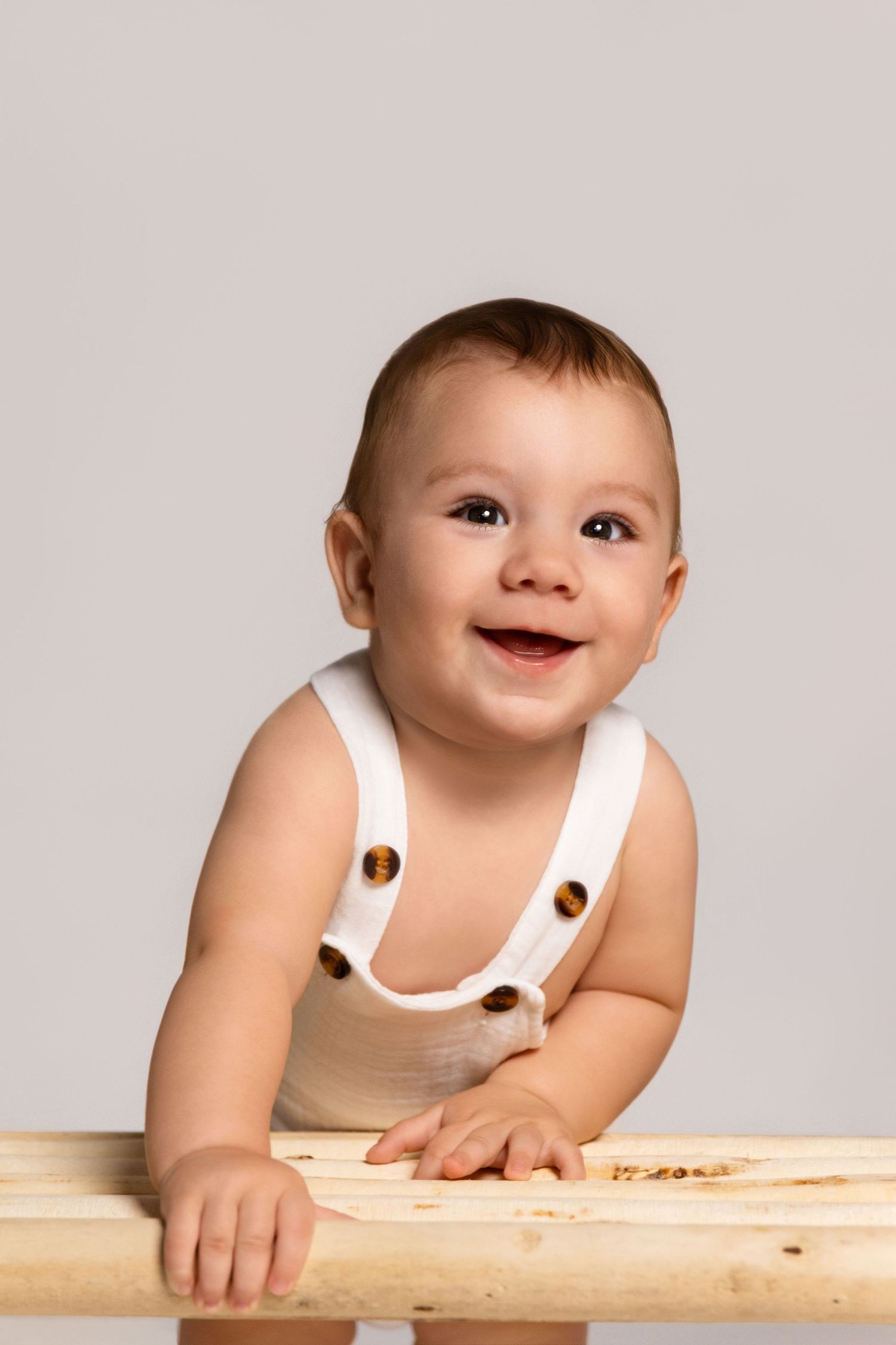 A heartwarming studio portrait featuring a white romper and wooden bench.