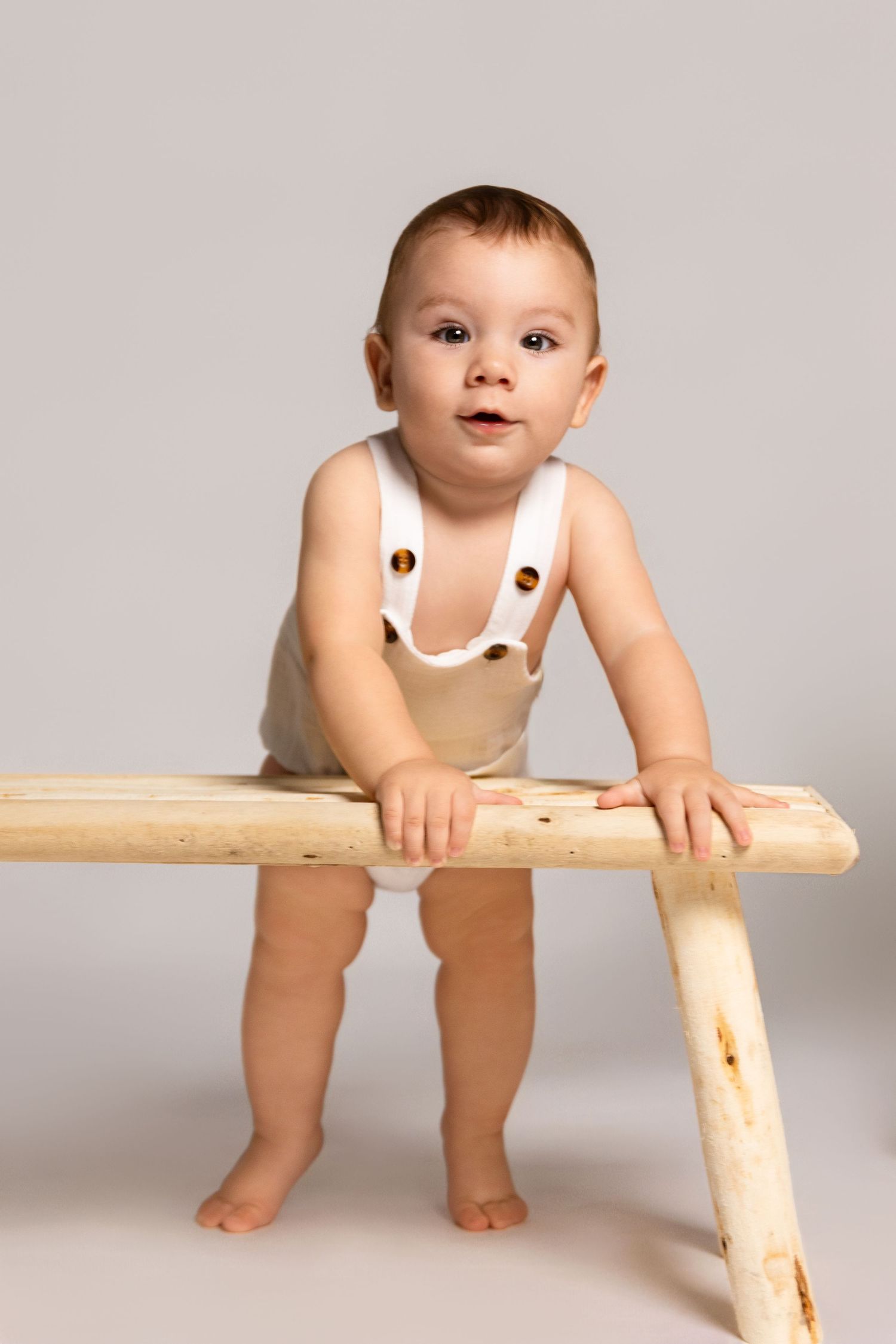 A playful studio portrait with natural wood elements and grey backdrop.