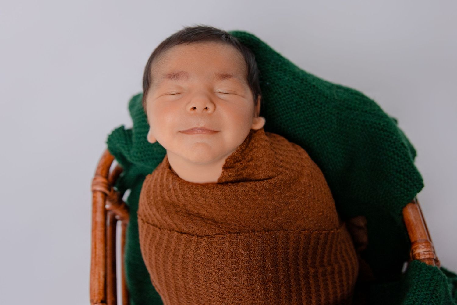 Newborn baby wrapped in brown and green knit blankets during professional photo session.