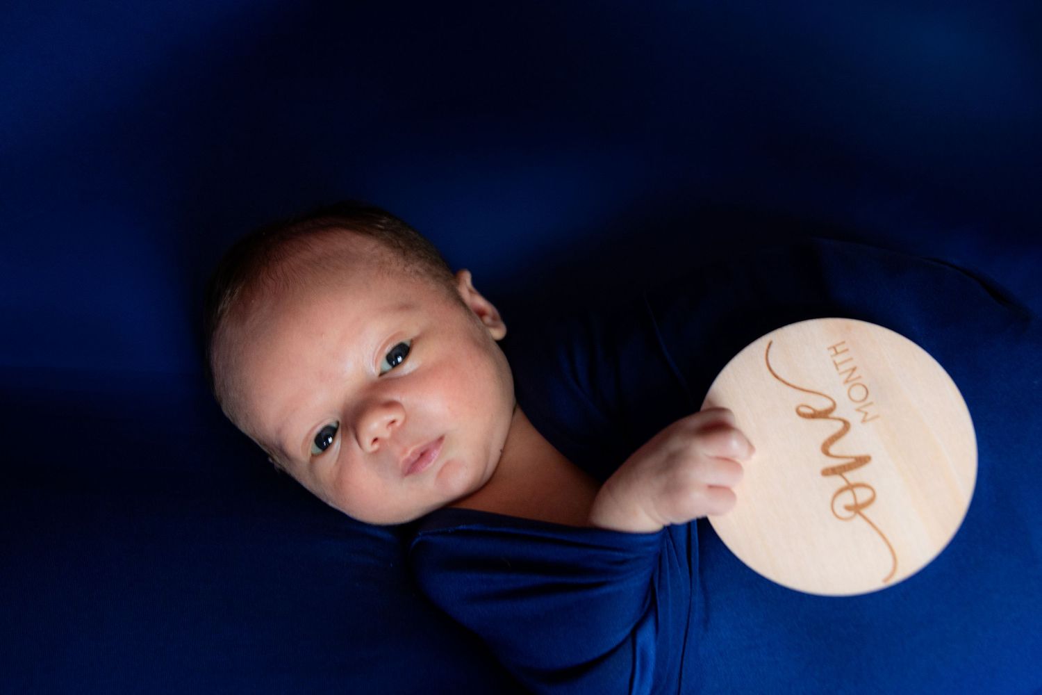 Artistic newborn photography against dark blue background with soft lighting effects.