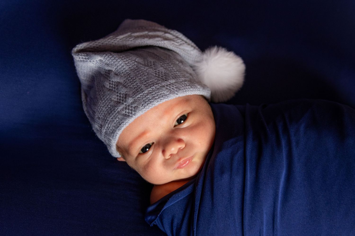 Low-key newborn portrait series with dramatic lighting against deep blue backdrop.