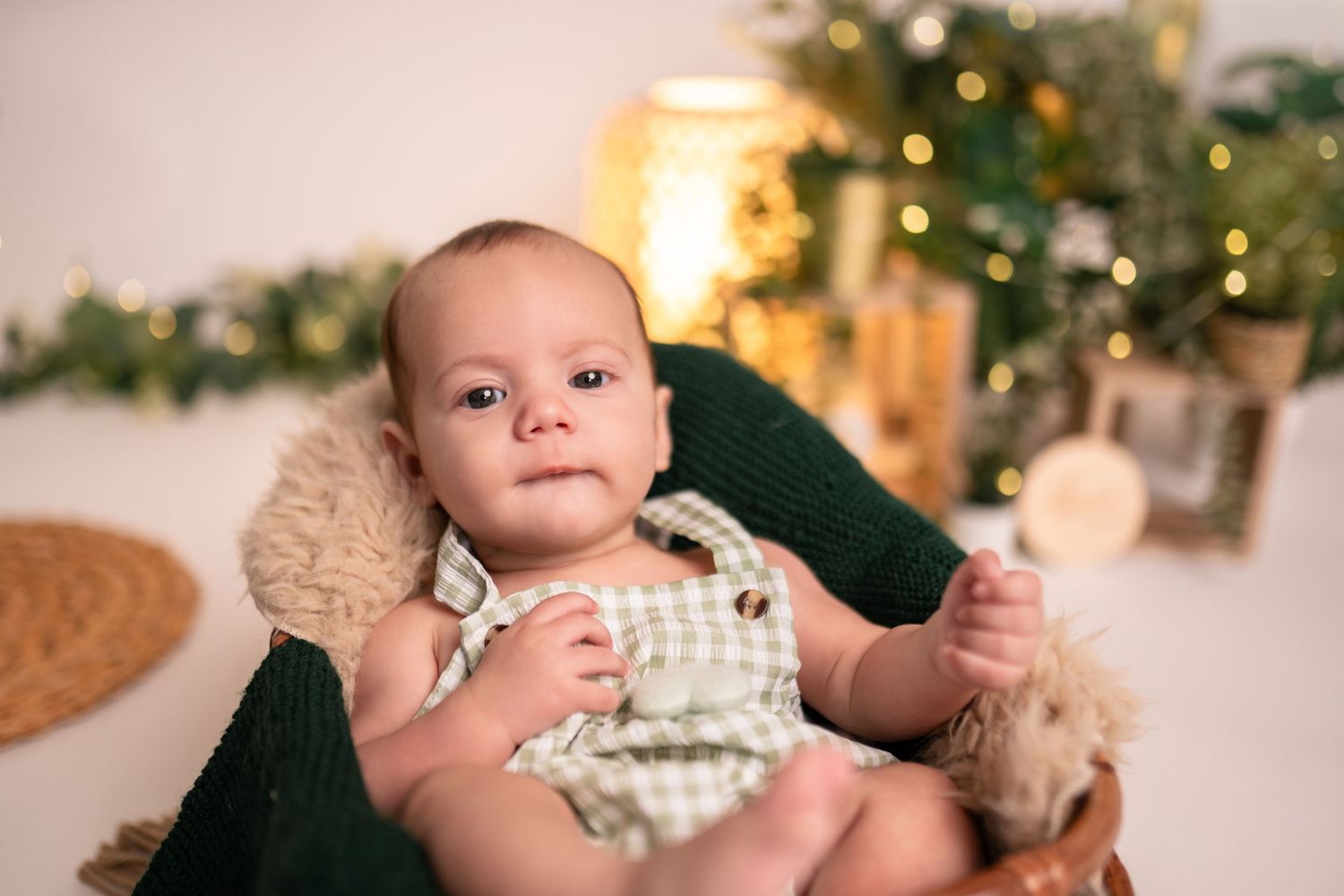 Baby portrait with warm holiday lighting and greenery decorations in background.