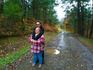 A wet forest trail winds through colorful autumn trees with puddles reflecting the fall foliage.
