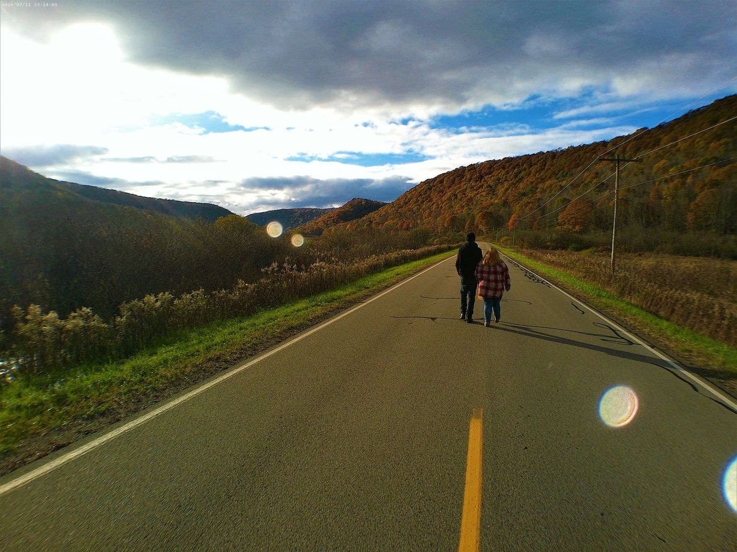 A scenic mountain road stretches into the distance with dramatic clouds and autumn foliage on the hillsides.