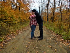 Two people share a moment on a leaf-covered forest trail during autumn.