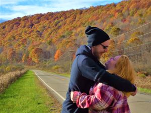 A romantic couple embraces on a scenic mountain road surrounded by autumn colors.