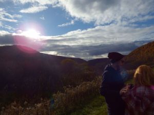A couple stands silhouetted against a dramatic sunset sky in the mountains.
