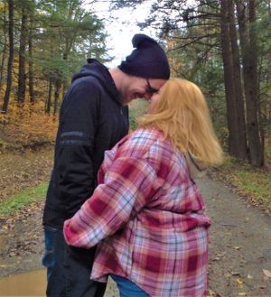 A couple shares a close embrace on an autumn forest path.