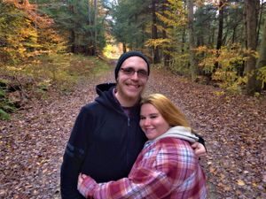 A couple embraces on a leaf-covered forest path during fall season.