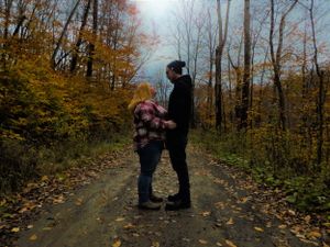 Two people walk together on a leaf-covered forest path during autumn.