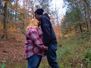 A couple shares a tender moment on a wooded trail surrounded by fall foliage.