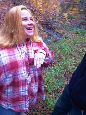Someone in a red plaid shirt smiles joyfully while walking through autumn woods.