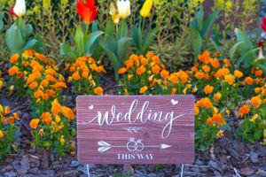 Rustic wooden wedding directional sign surrounded by colorful spring flowers.