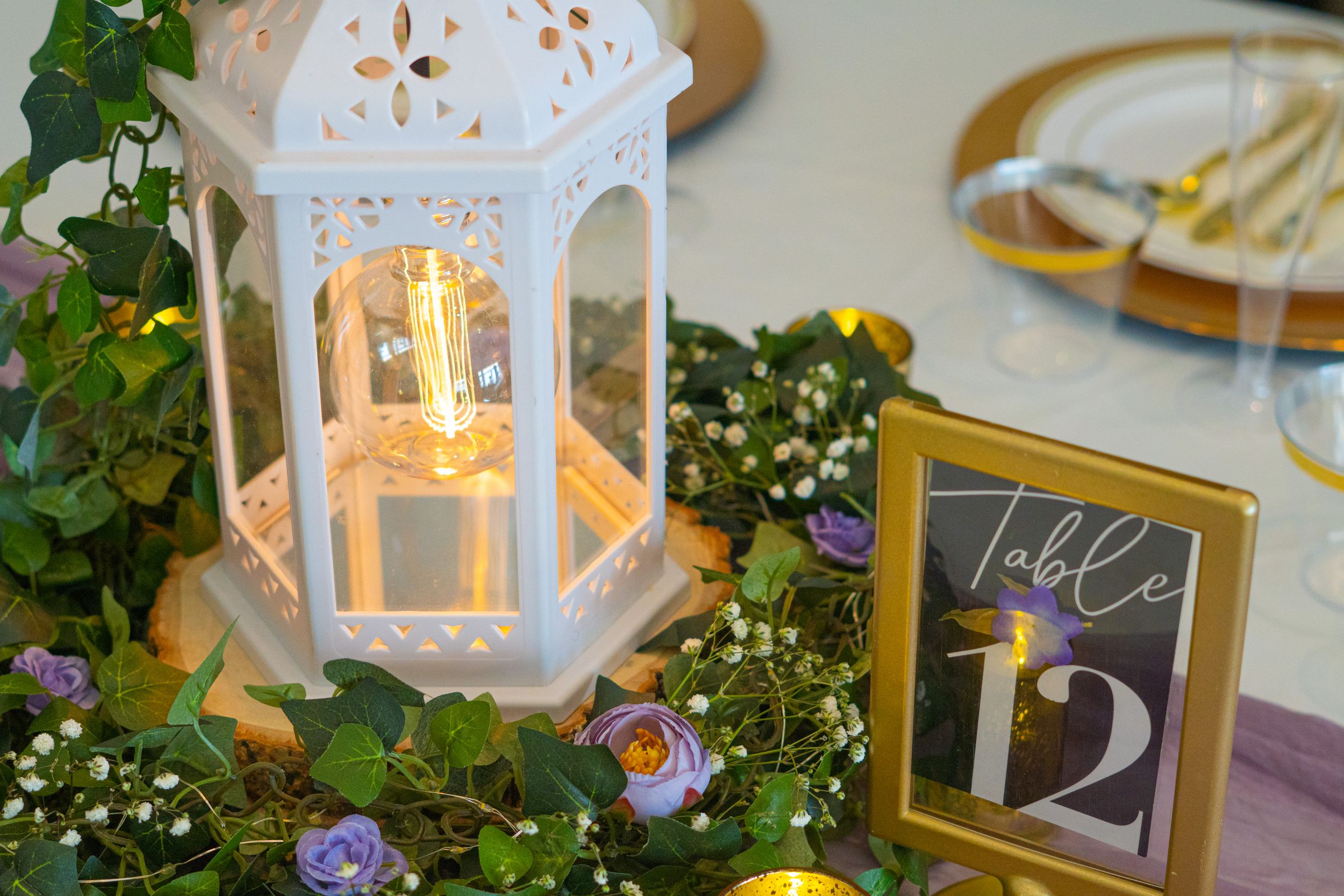 White decorative lantern and table number 12 surrounded by delicate floral arrangements.