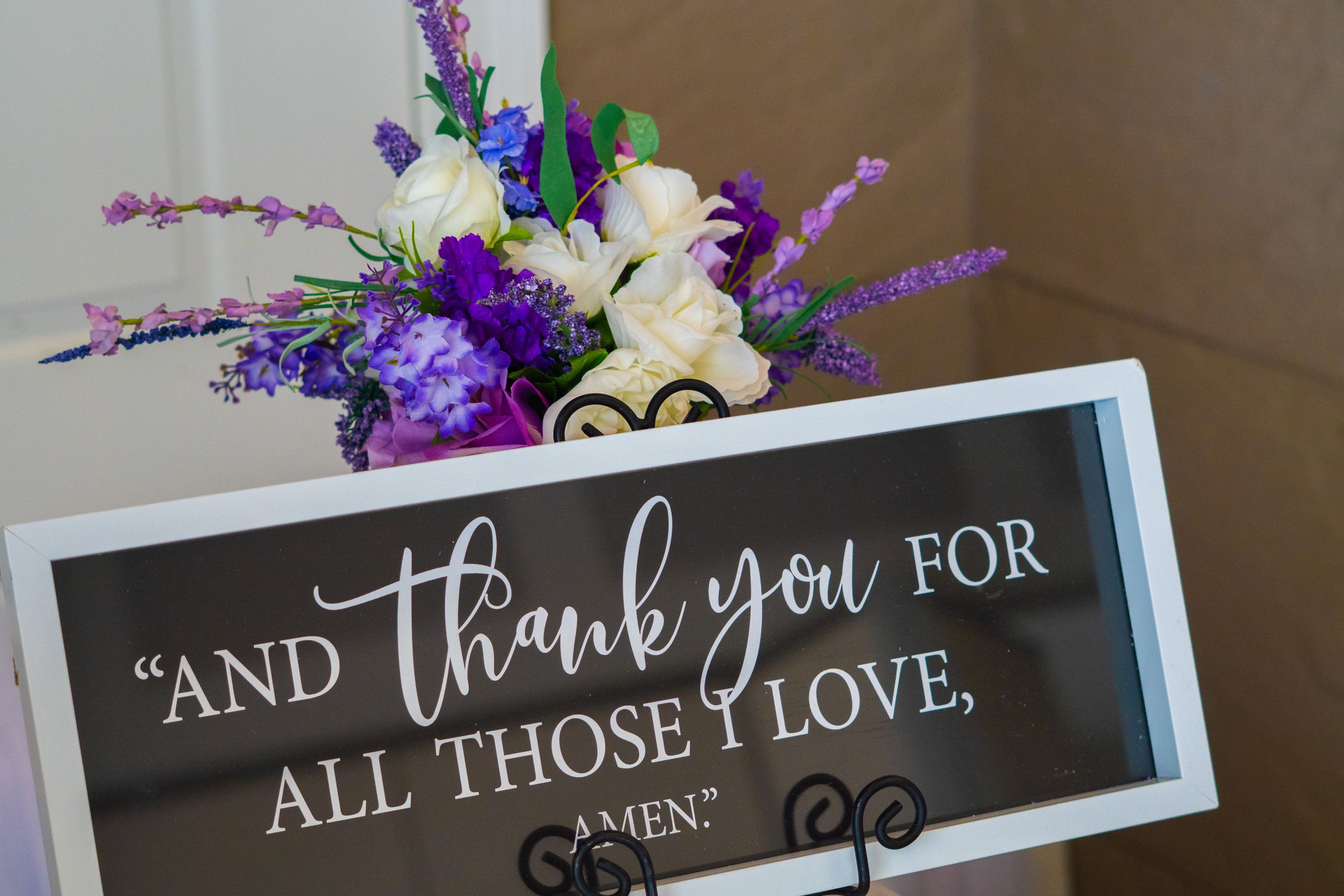 Wedding decor featuring purple and white floral arrangement with a framed thank you message.