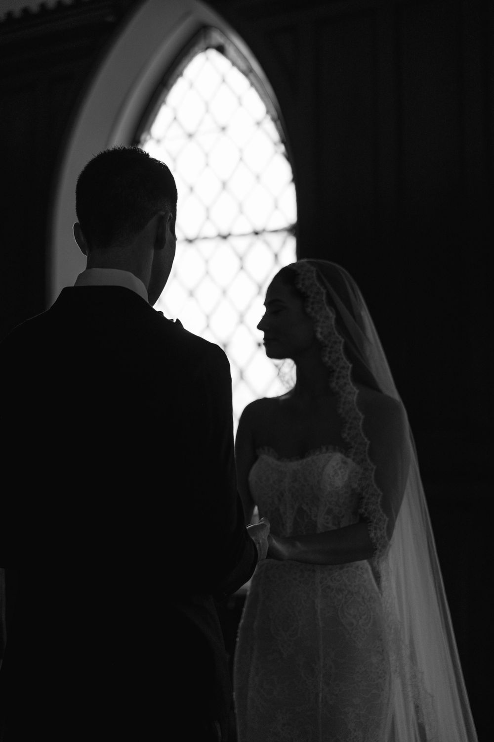 Silhouetted couple against church window in romantic black and white wedding photo.