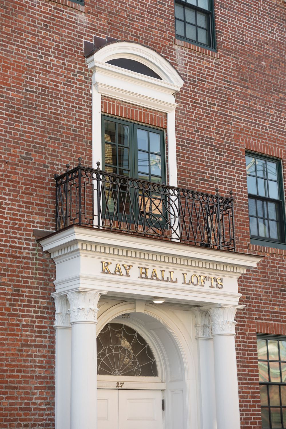 Entrance to Kay Hall Lofts featuring ornate brickwork, white columns, iron balcony and arched architectural details.