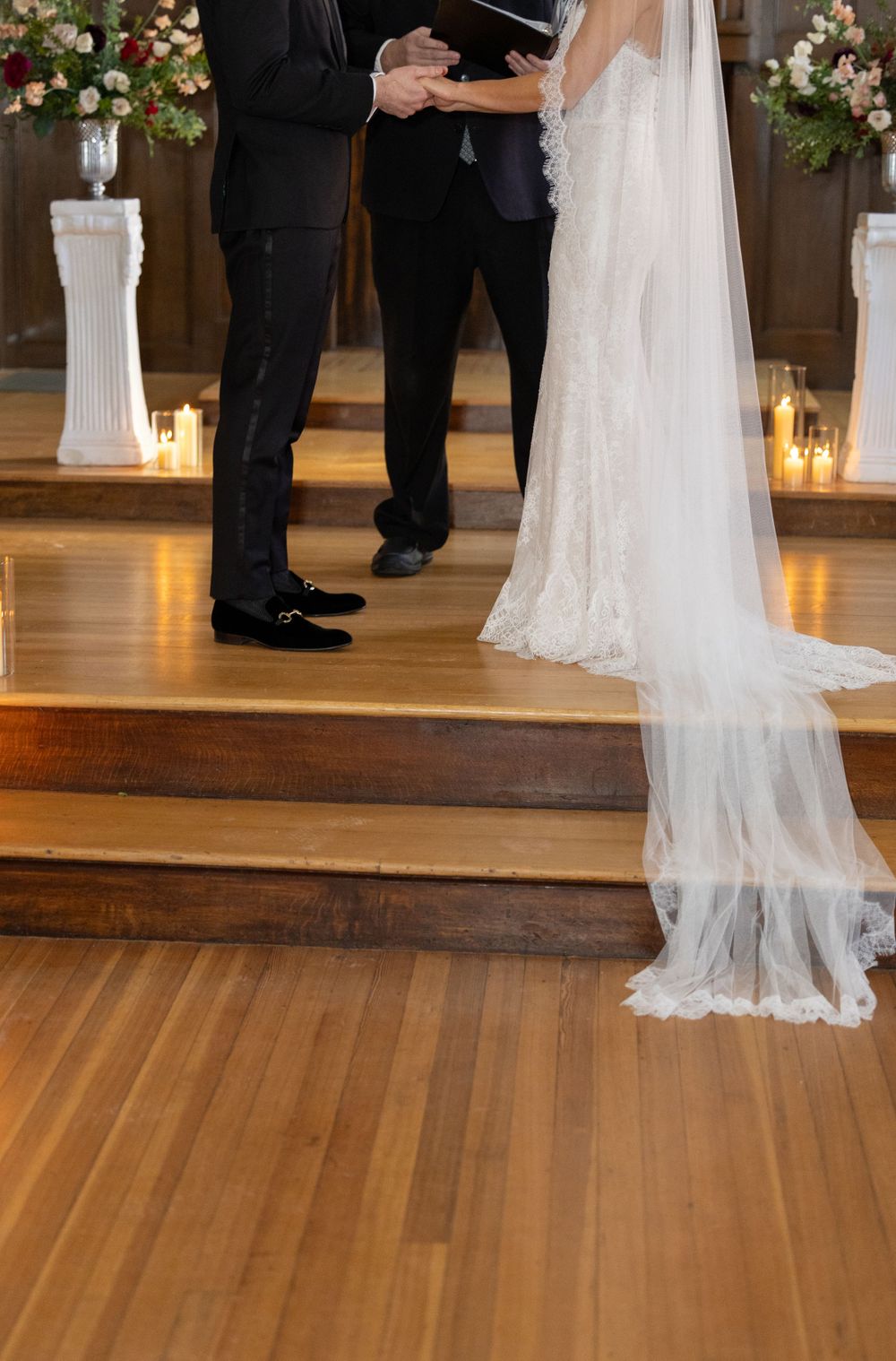 A close-up of wedding ceremony details showing flowing white bridal veil and formal attire on wooden flooring.
