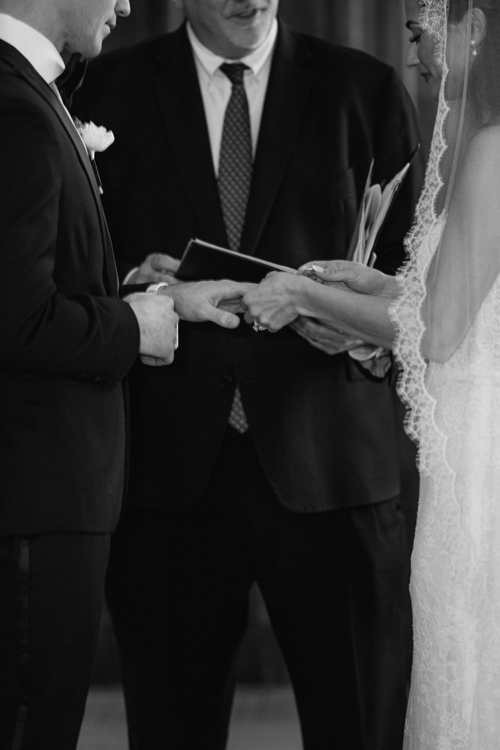 Black and white photo of a wedding ceremony exchange of rings with an officiant during the vows.