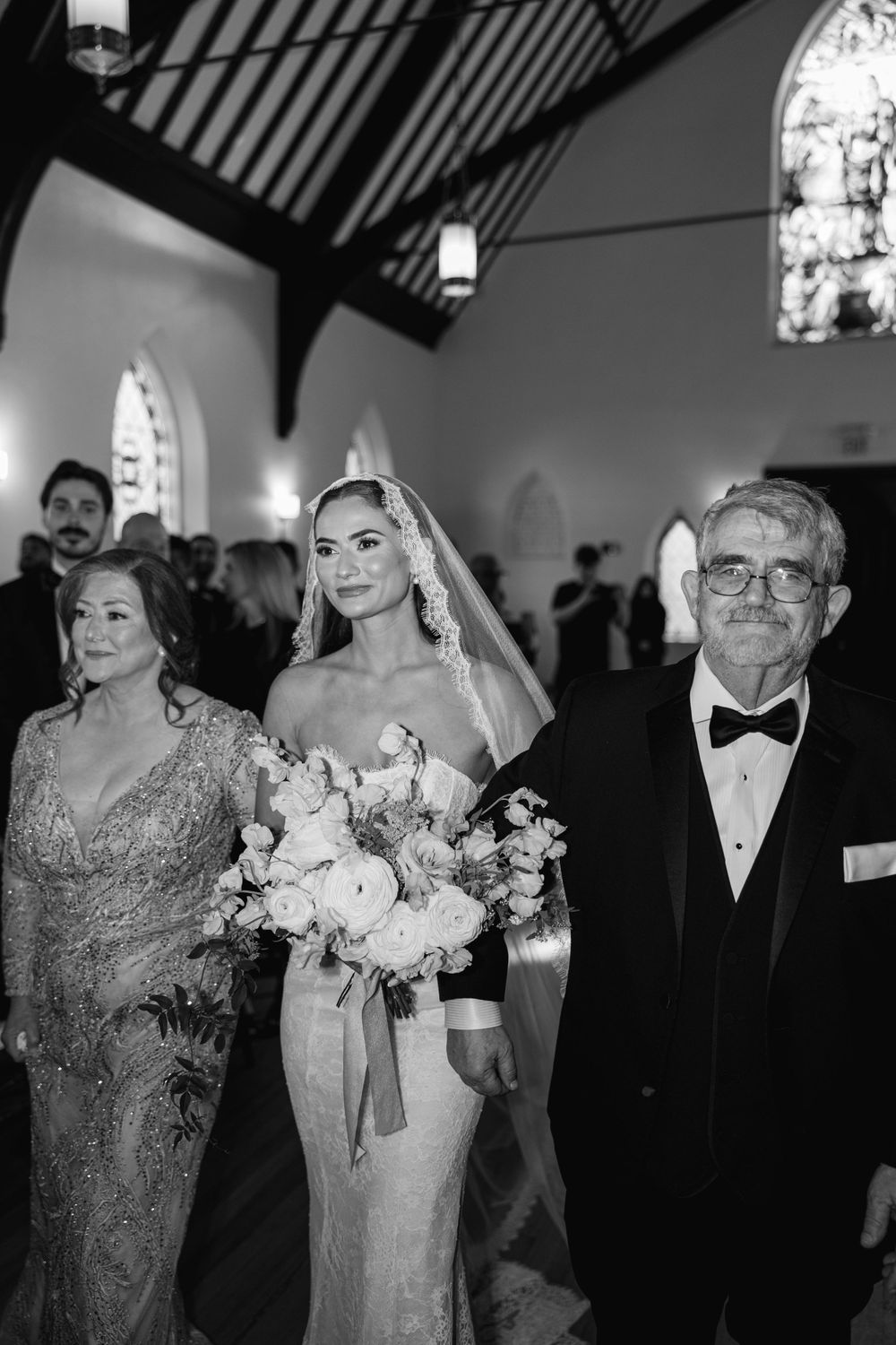 Wedding party photo in church with bride holding white bouquet surrounded by family.