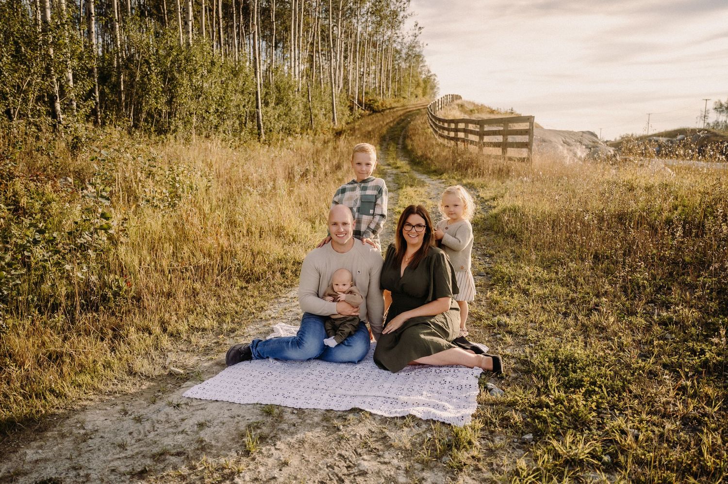 A family sits together on a blanket on a grassy hillside path during golden hour.