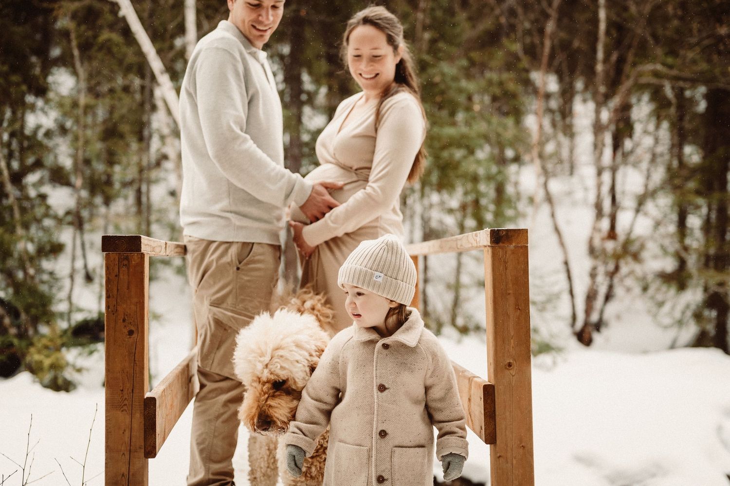 Winter family portrait in snow with young child and teddy bear.