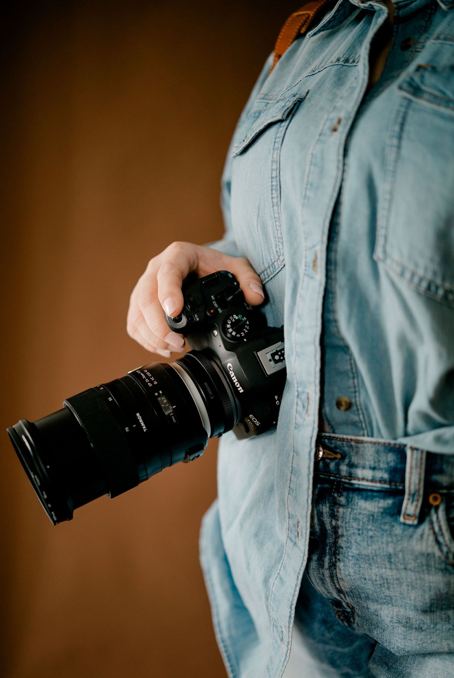 Close-up of woman in denim shirt holding a Canon DSLR camera with zoom lens.