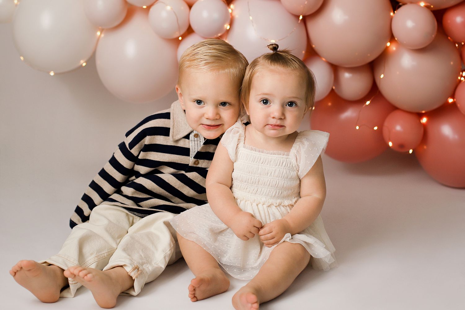 Six connected photos show babies sitting against a pink balloon backdrop in coordinating white and striped outfits.