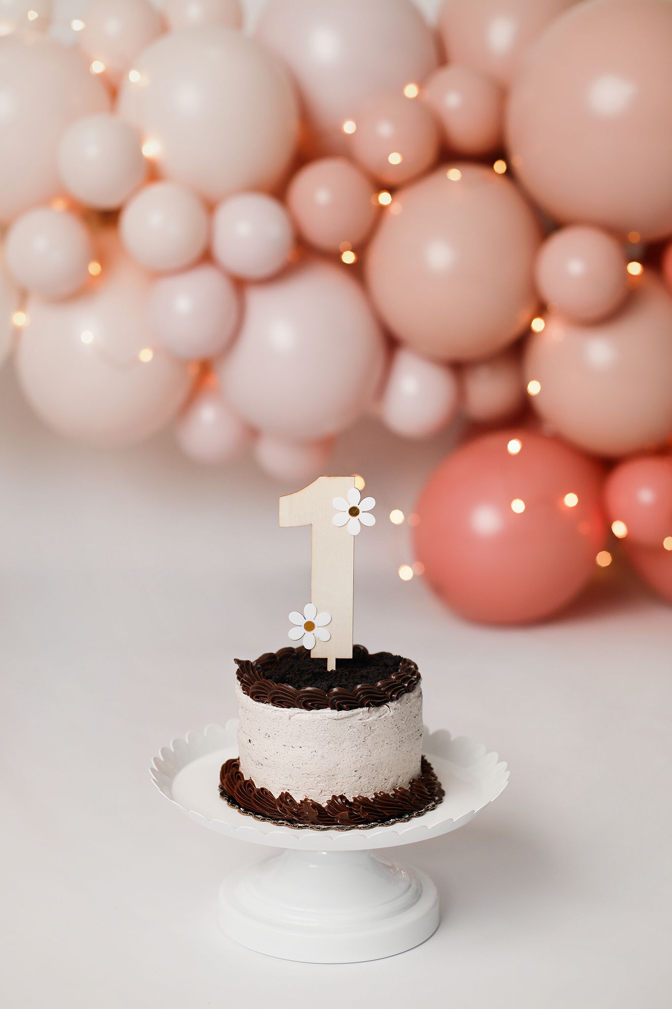 A black and white smash cake with number one candle against blush pink balloon garland backdrop.