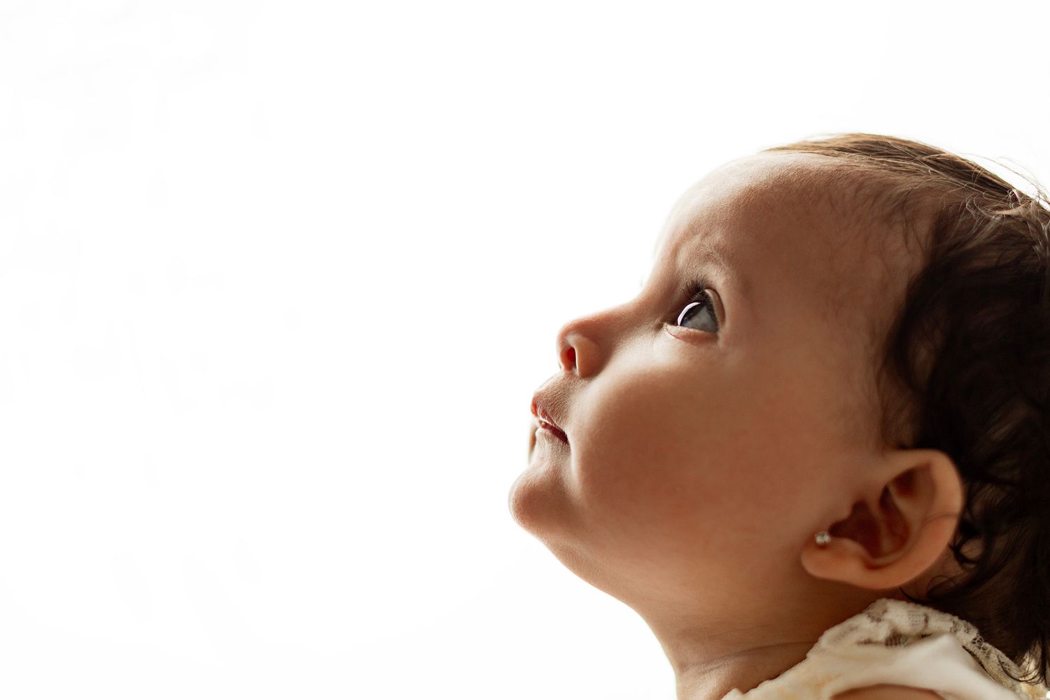 Close-up profile of a curious baby looking upward against a white background.