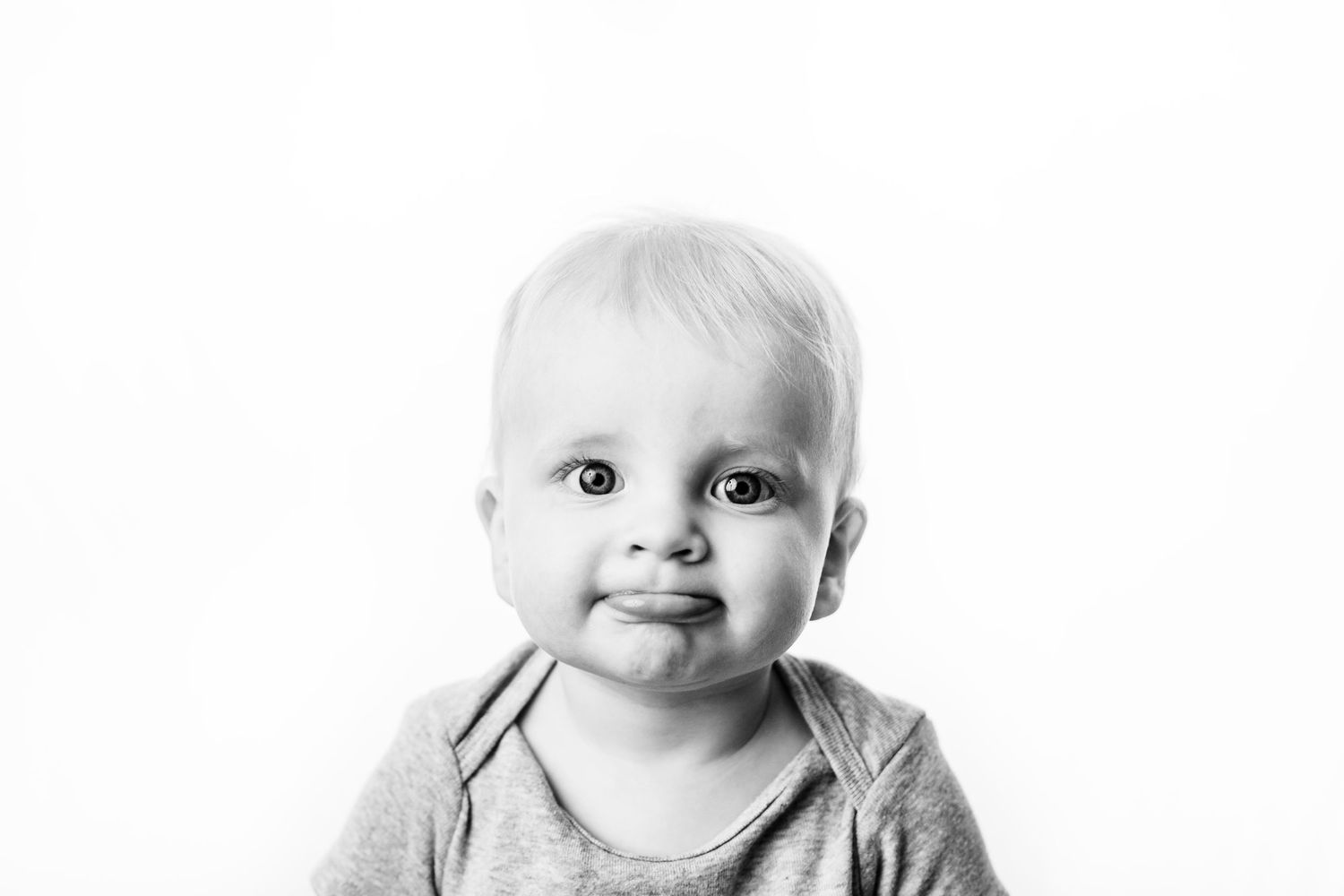 Adorable baby with big eyes and light hair smiling in a black and white portrait photo.
