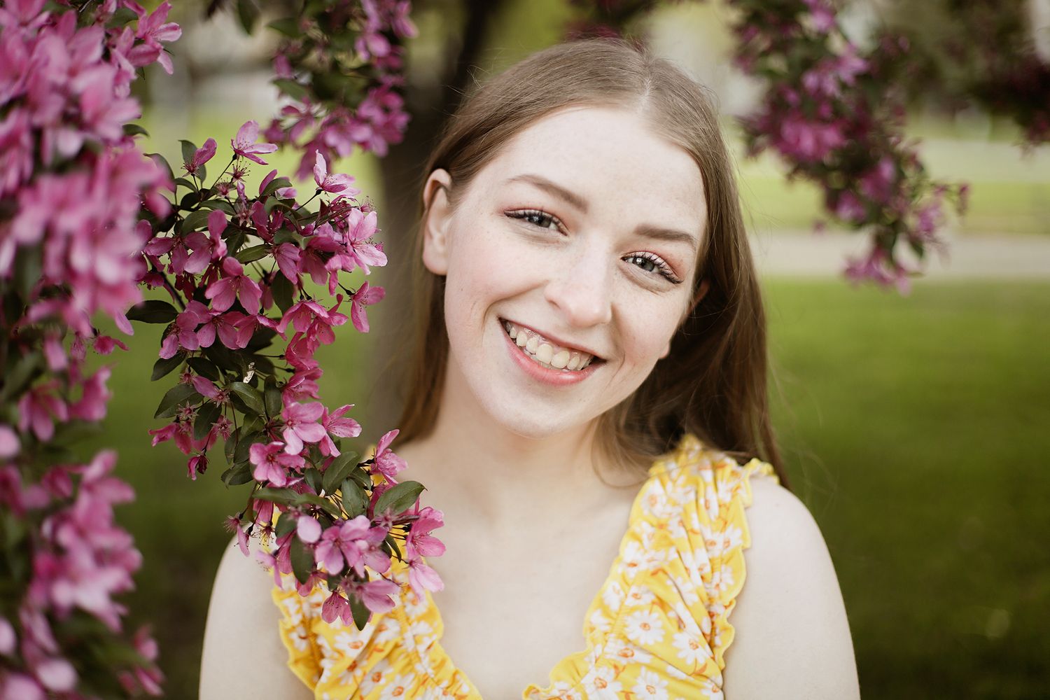 A bright spring portrait with pink crabapple blossoms and a yellow floral dress against a soft green background.