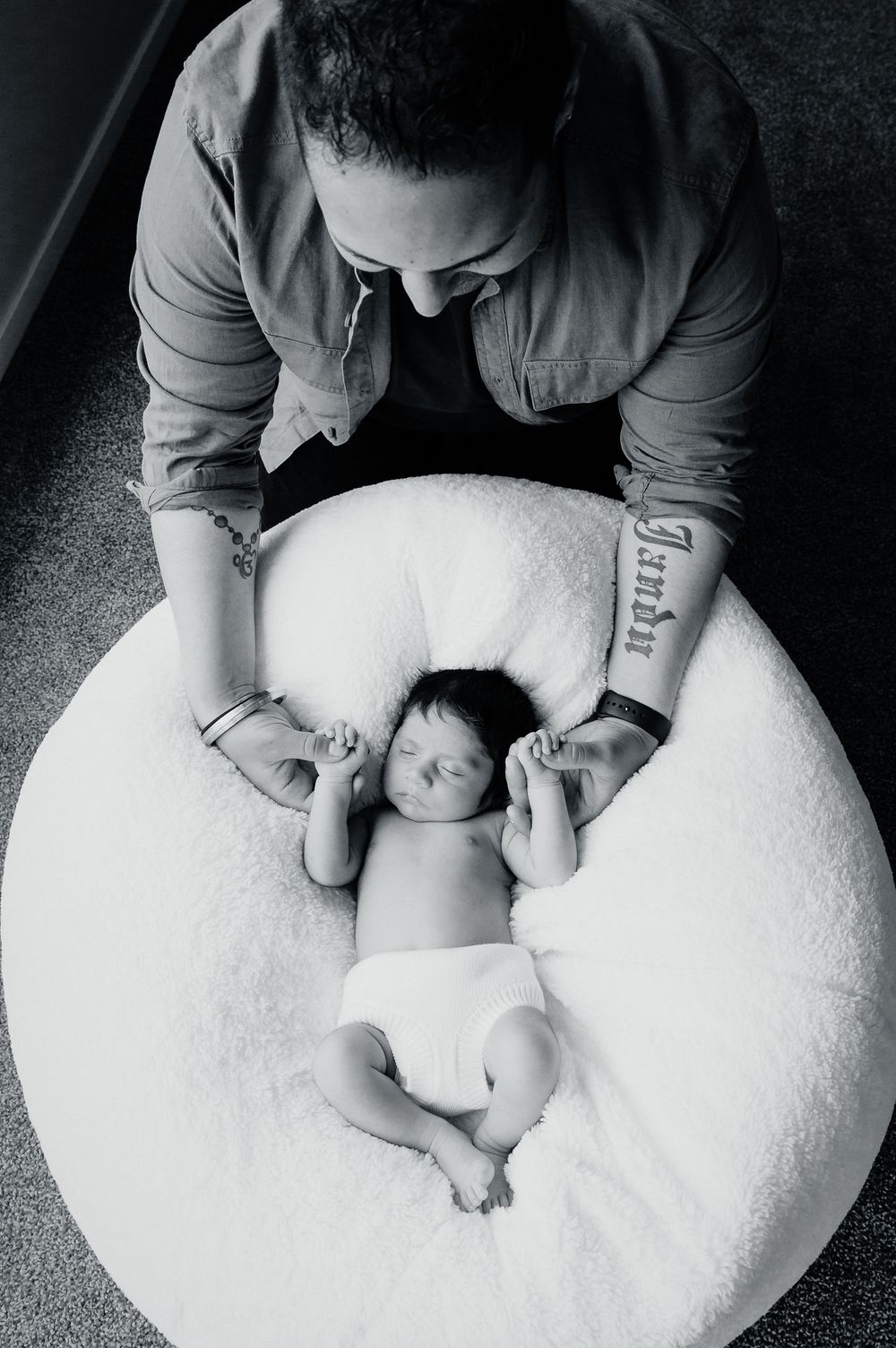 Black and white photo of a sleeping newborn baby on a round white cushion with caregiver holding their feet.
Altona Family Photography
