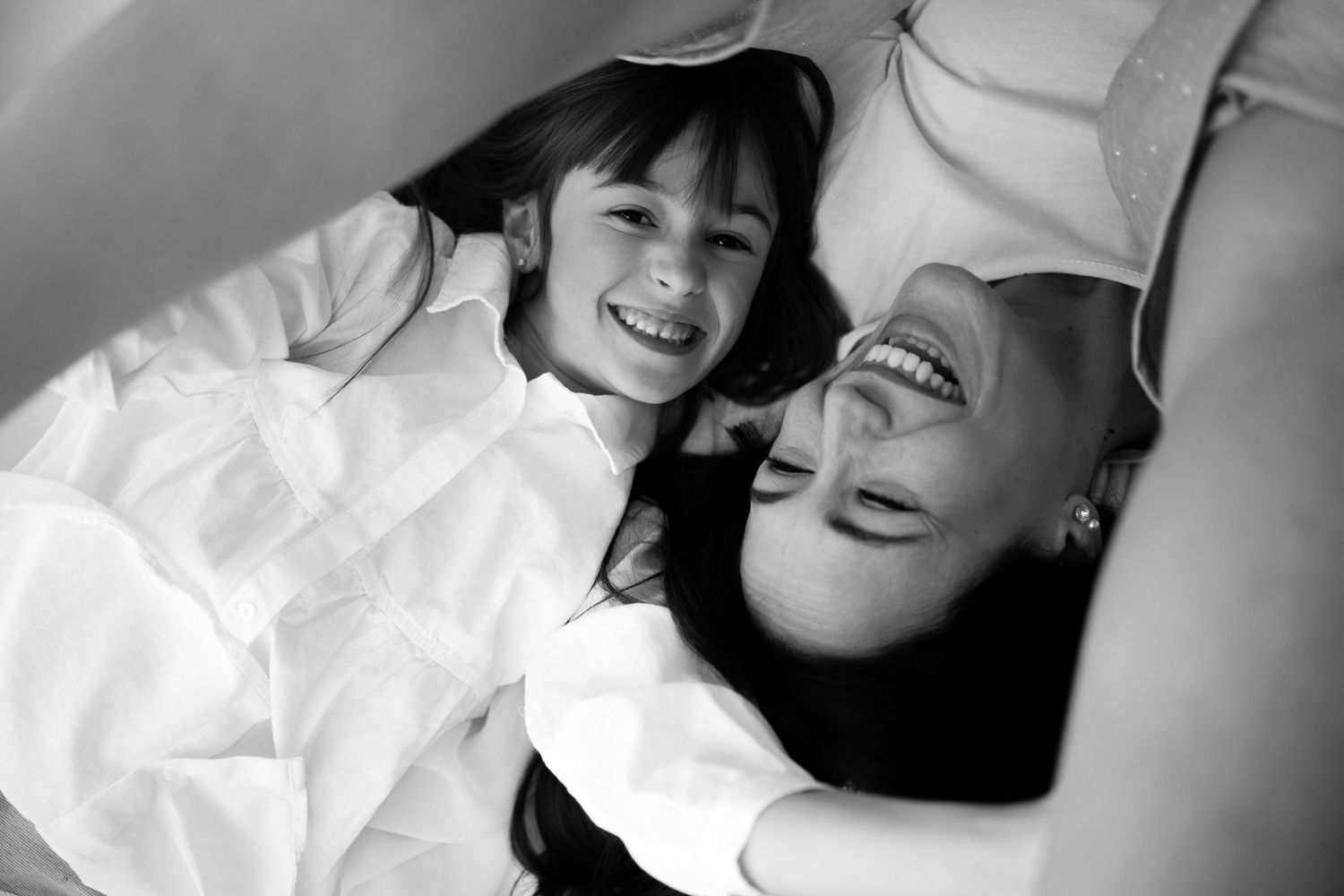 Black and white photo of mother and daughter laughing joyfully together on a bed.