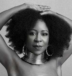 Black and white portrait showcasing natural afro hair and metallic choker necklace against simple background.
