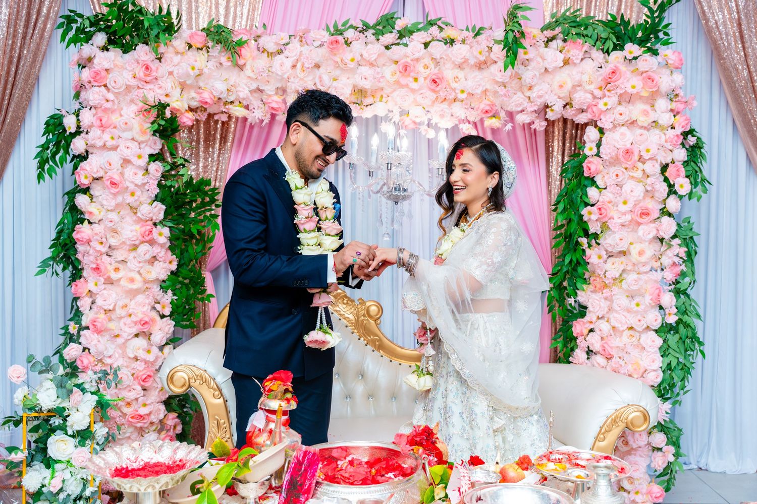 Couple sharing a special moment with gifts under pink flower-adorned wedding arch.
