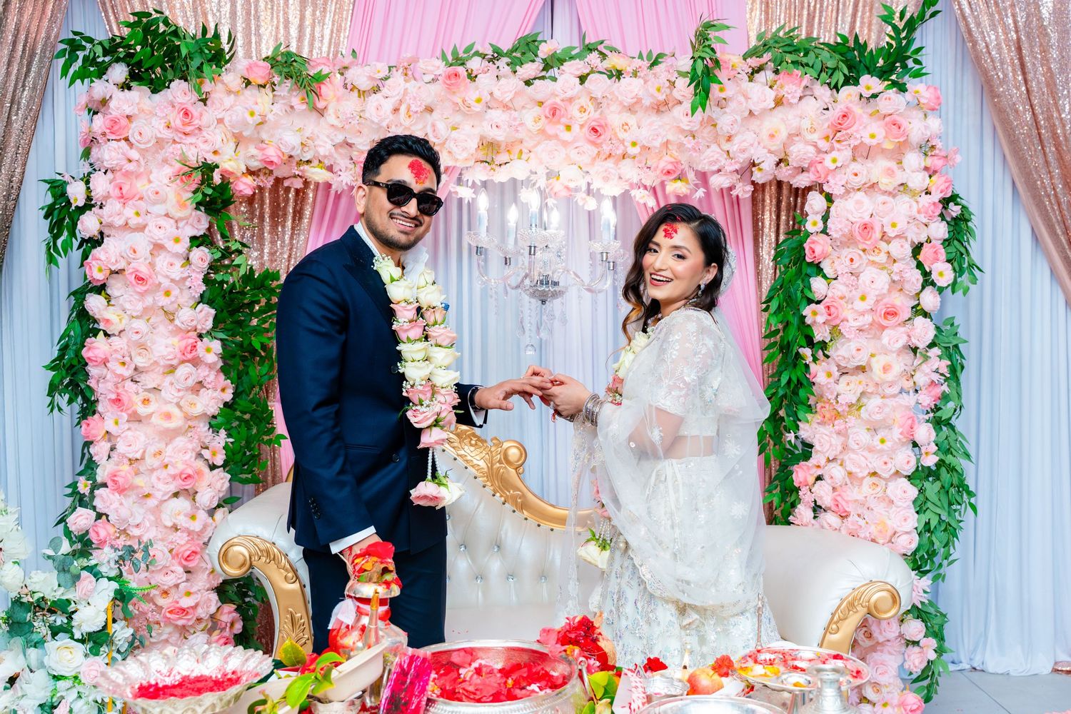 Festive wedding moment captured under ornate pink flower arch with decorative details.