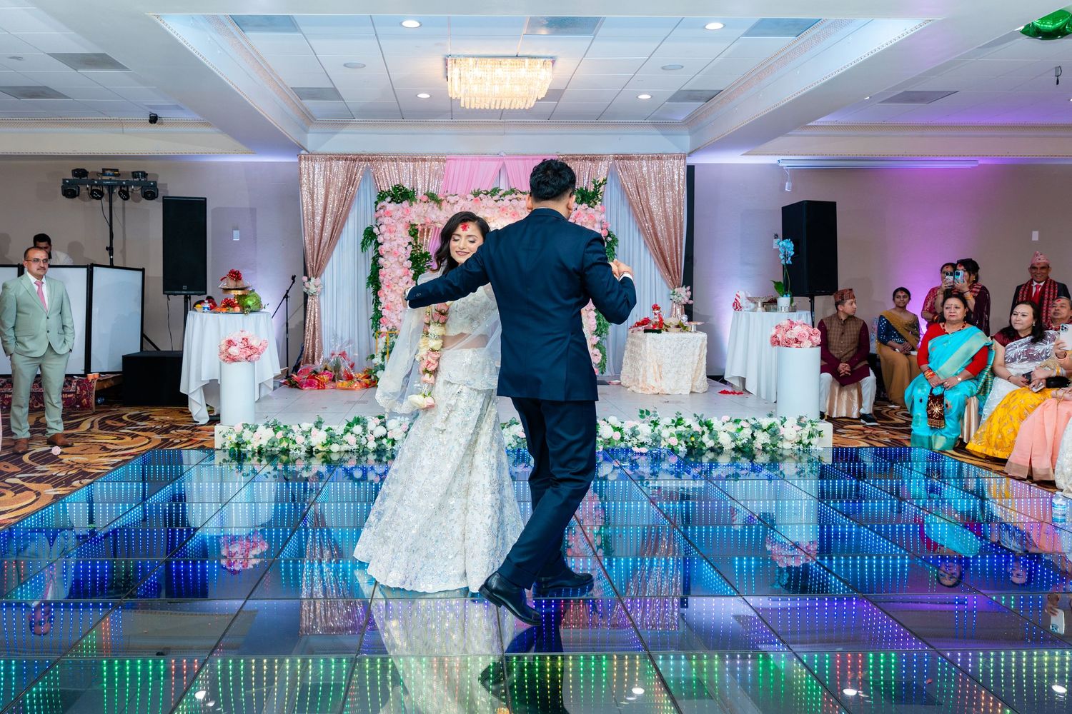 Newlyweds dancing together on an illuminated blue dance floor surrounded by floral decorations.