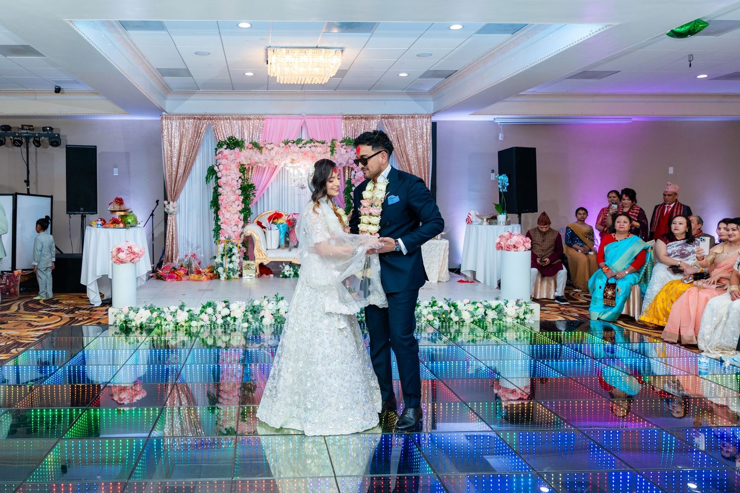 Romantic wedding dance moment captured on a light-up floor with pink floral arch backdrop.