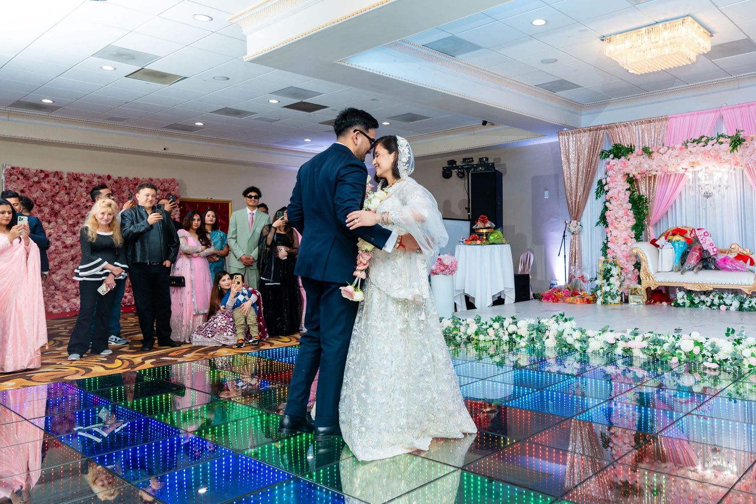 Wedding celebration features couple dancing on reflective LED floor with pink decor and lighting.