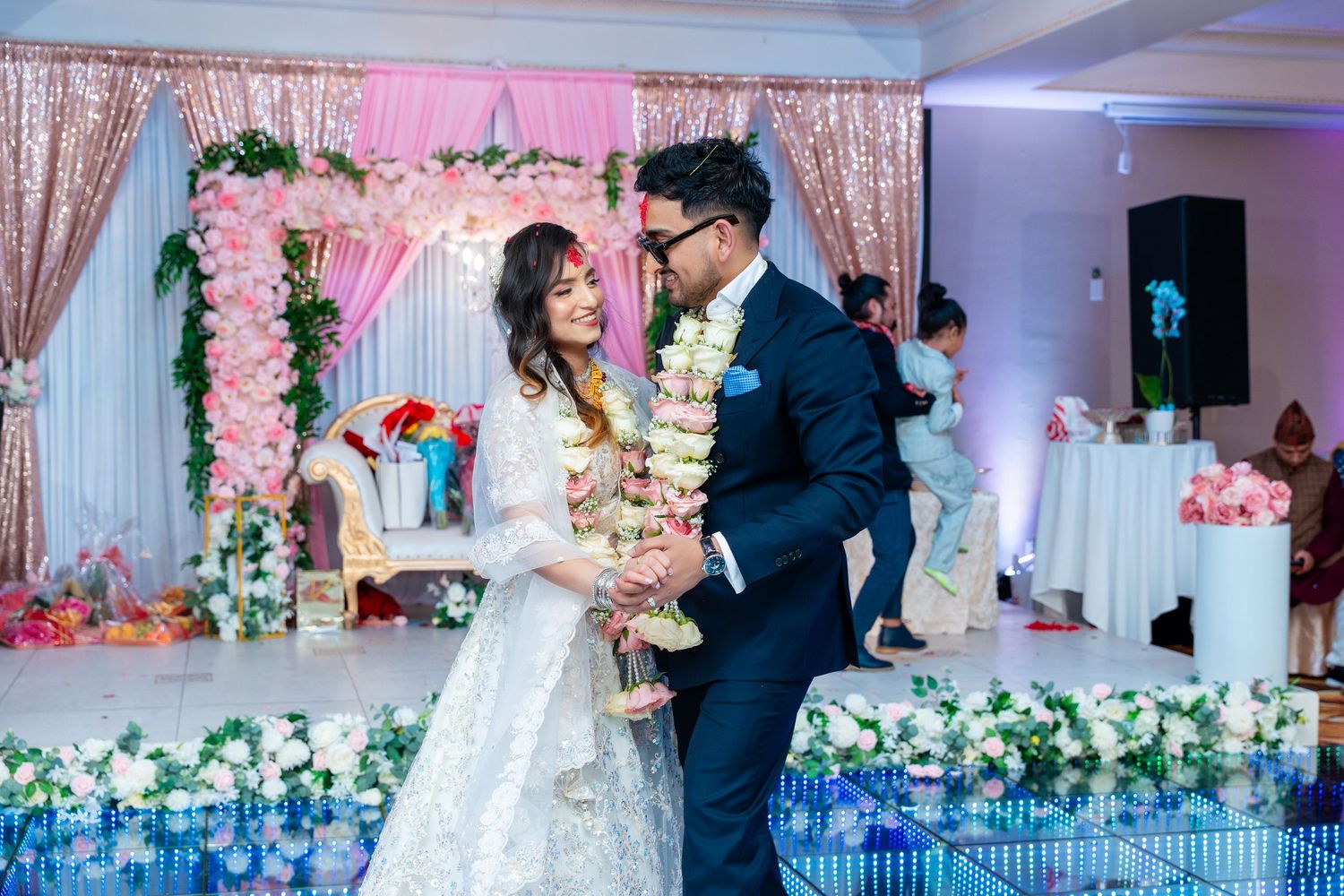Couple shares intimate dance moment under pink floral arch with LED floor lighting effects.