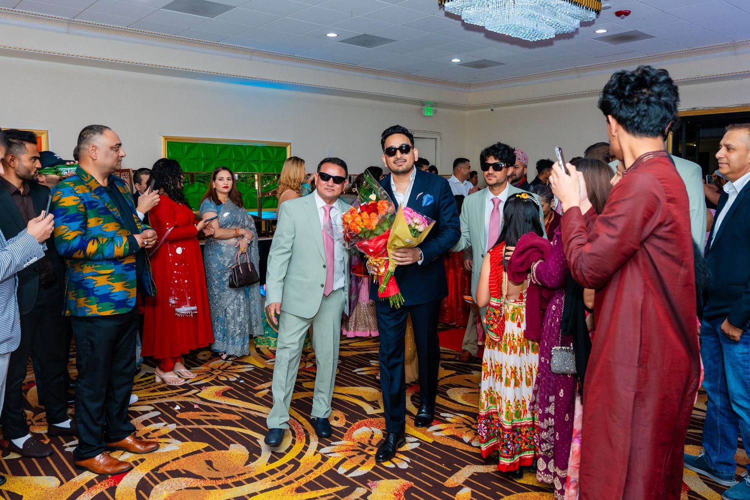 Indoor celebration with guests in colorful formal attire on patterned carpet.