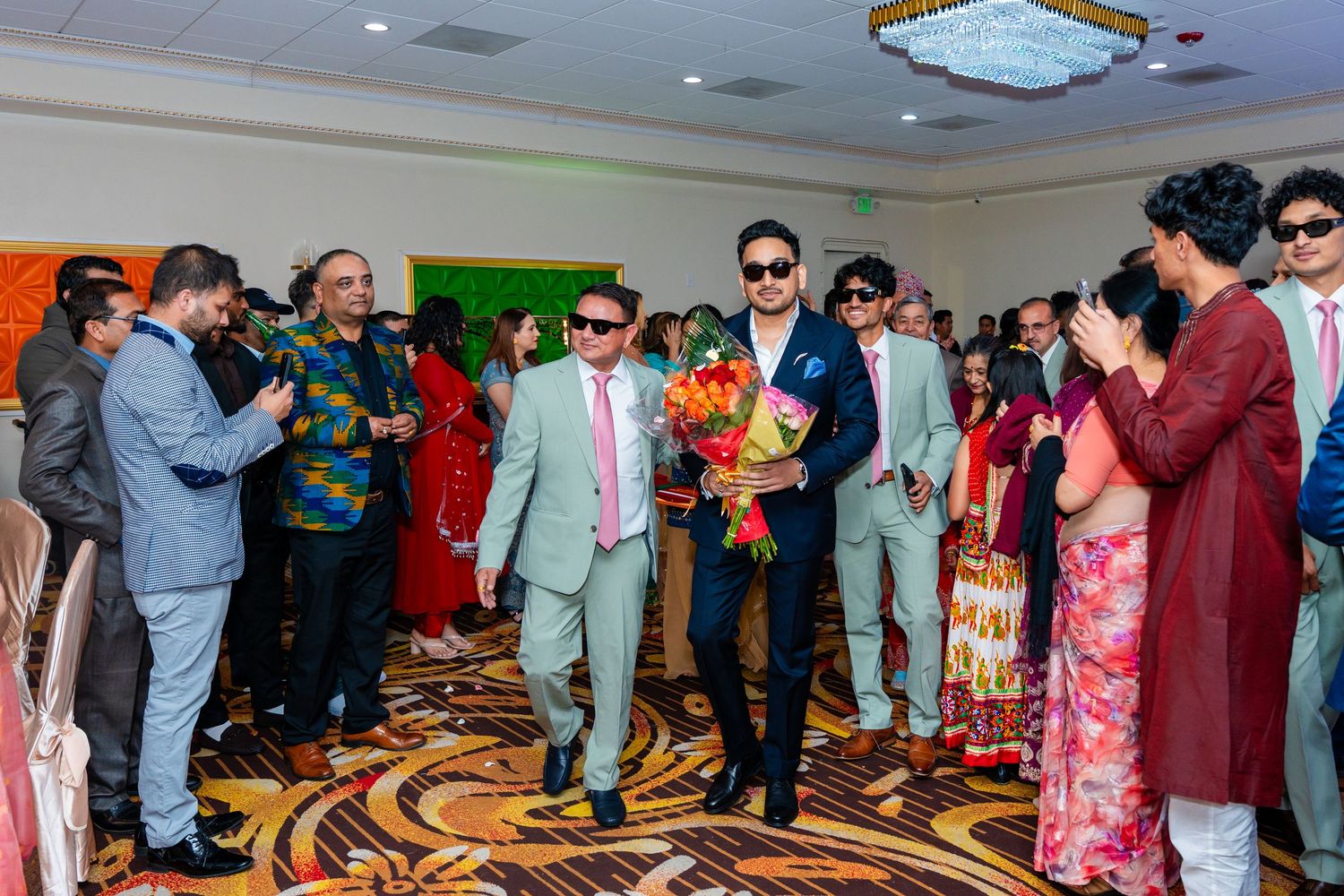 Group celebration scene with guests in suits walking on decorative carpeted floor.