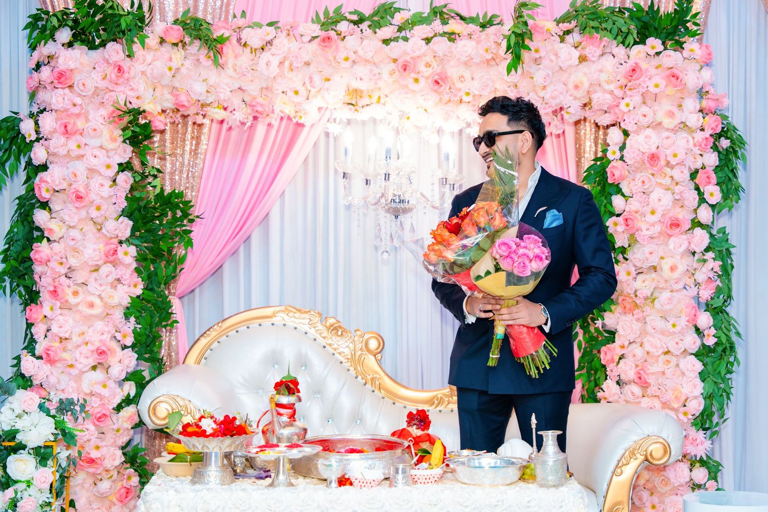 A romantic wedding scene with a pink floral arch and ornate white throne setup for a celebration.