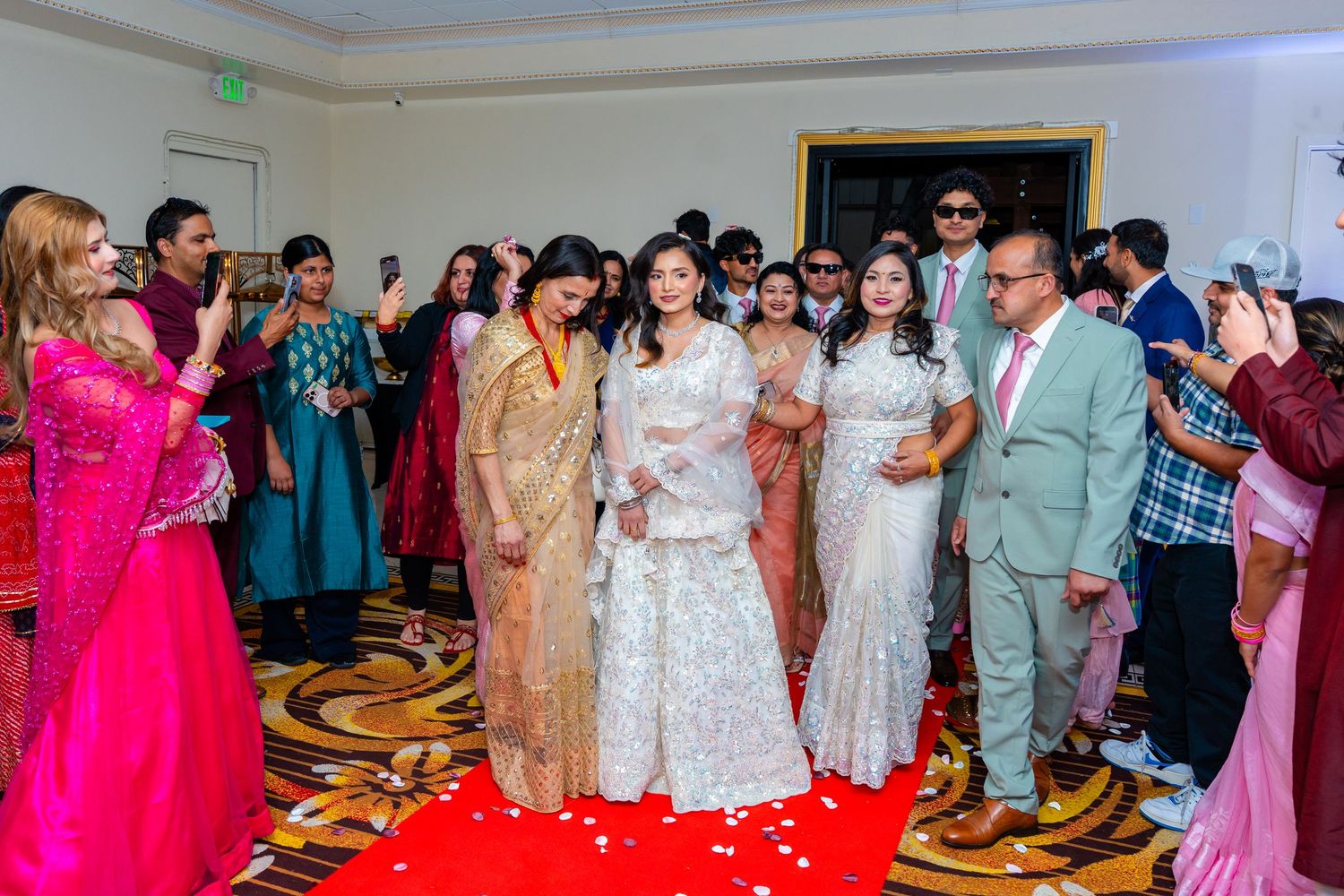 Wedding celebration with guests in colorful attire standing on a red carpet in an elegant ballroom.